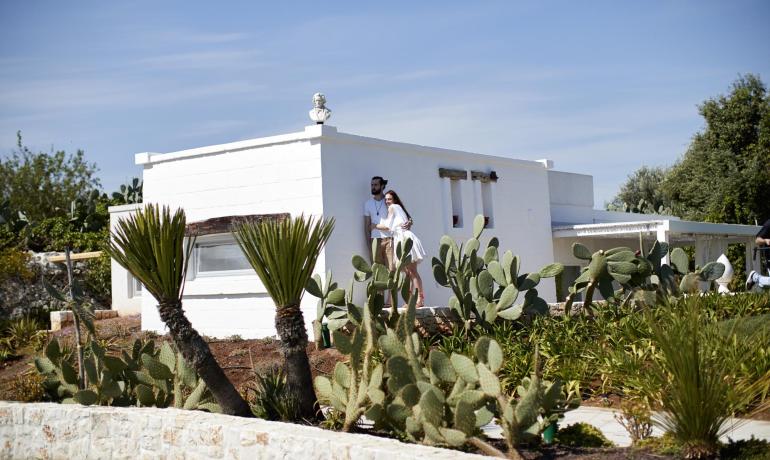 Coppia davanti a casa bianca circondata da cactus e palme.